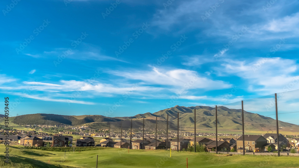 Pano Golf course fairway and putting green with flagsticks under blue sky and clouds