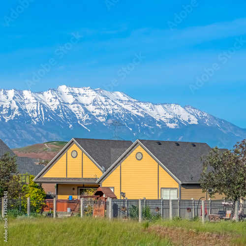 Square frame Single storey houses against striking snow capped mountain and vibrant blue sky © Jason