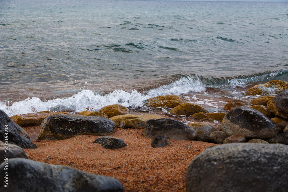 Stones on the sea beach. Pasture winter day. Clear water and sand. Kyrgyzstan, Issyk-Kul Lake Stones on the sea beach. Pasture winter day. Clear water and sand. Kyrgyzstan, Issyk-Kul Lake