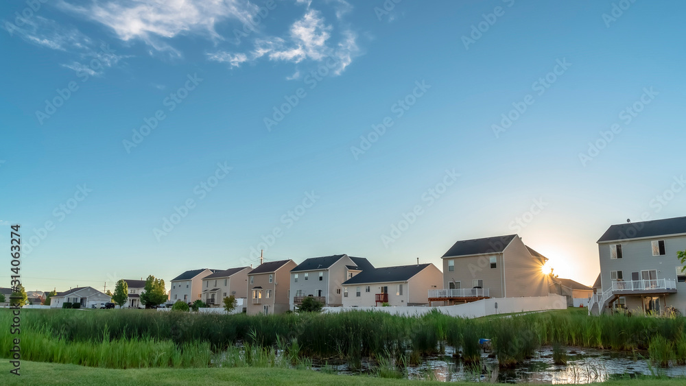 Pano frame Sunset views in the suburb with pond and houses against bright sun and blue sky