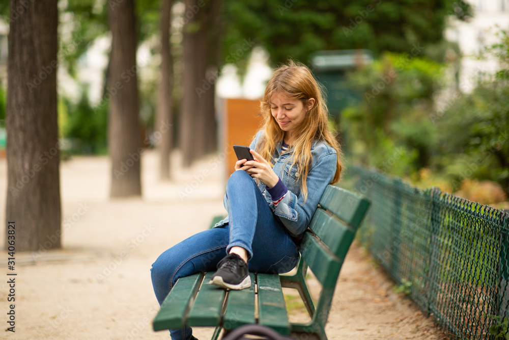 young woman sitting on park bench looking at cellphone young woman sitting on park bench looking at cellphone