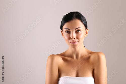 Portrait of young beautiful woman with perfectly clean face skin. Female with long black hair tied in ponytail smiling showing skincare results. Close up, copy space background.