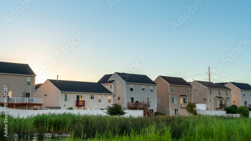 Pano frame Facade of houses in the suburb with view of green grassy terrain and shiny pond