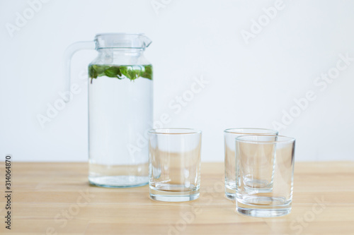 carafe with water and mint and several glass glasses on a wooden table with a light background