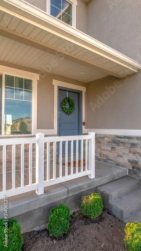 Vertical frame Home facade with small porch and blue gray front door with green leafy wreath