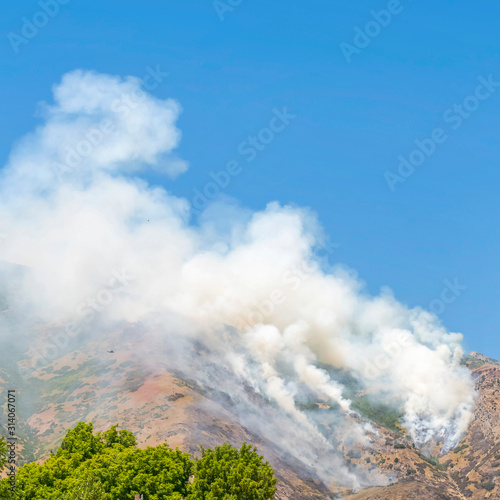 Square frame Wild forest fire in the mountain emitting thick white smoke against blue sky