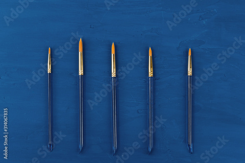 Blue paint brushes on classic blue background, view from above