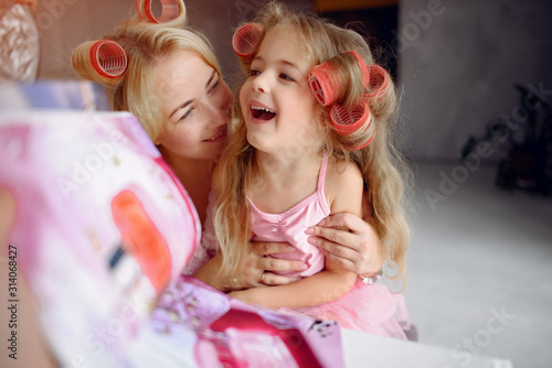 Family sitting in a room. Mother in a pink pajamas. Mom and daughter with curlers on their heads