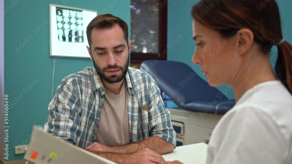 A focused serious female doctor is talking about a patient's medical history while sitting with a patient by the table at the hospital A focused serious female doctor is talking about a patient's medical history while sitting with a patient by the table at the hospital