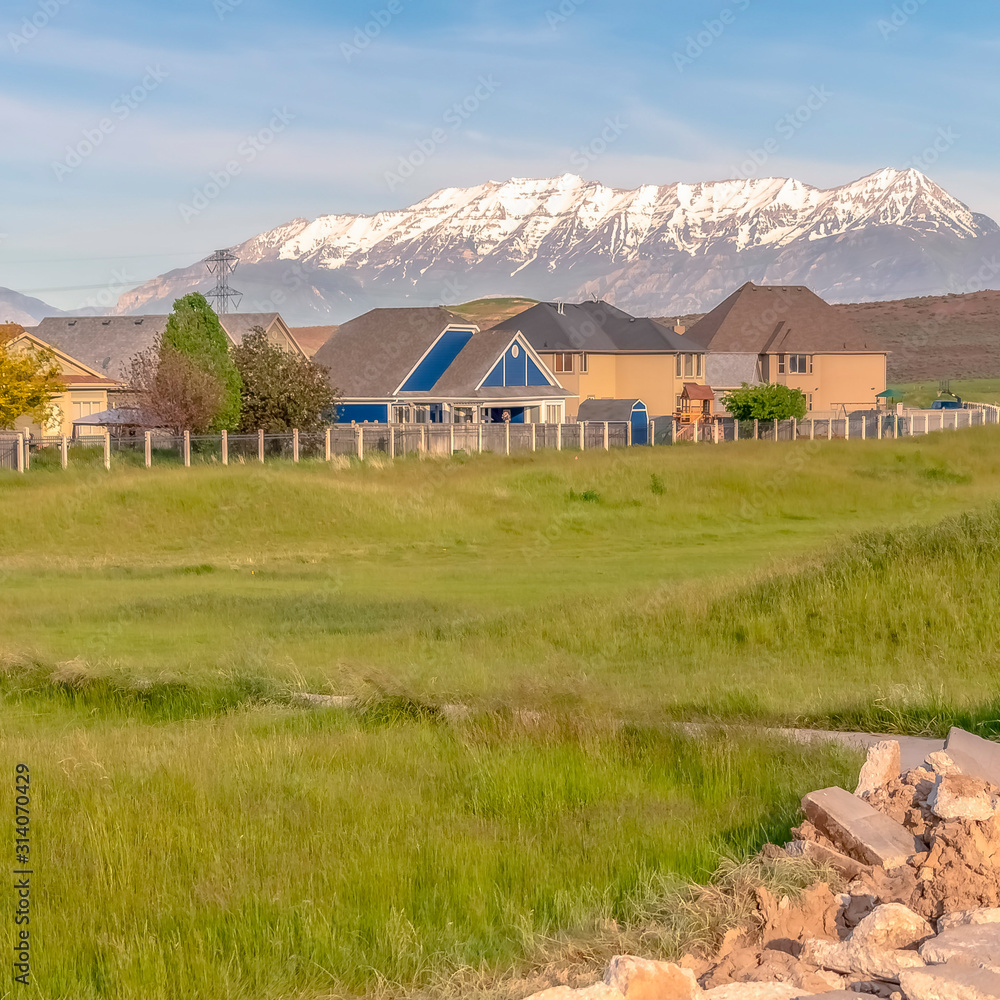 Square Damaged curving road amid grassy terrain against homes and snow capped mountain Square Damaged curving road amid grassy terrain against homes and snow capped mountain