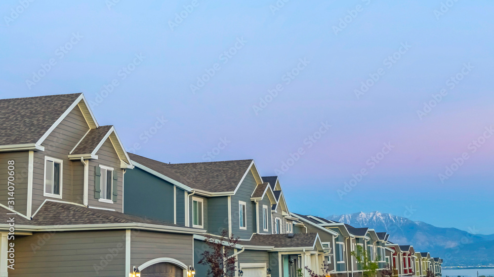 Pano frame Exterior of homes with gable and valley roofs against mountain and sky at sunset