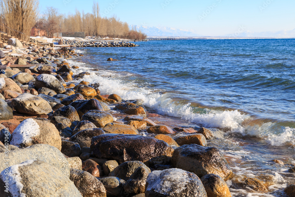 Stones on the sea beach. Pasture winter day. Clear water and sand. Kyrgyzstan, Issyk-Kul Lake Stones on the sea beach. Pasture winter day. Clear water and sand. Kyrgyzstan, Issyk-Kul Lake