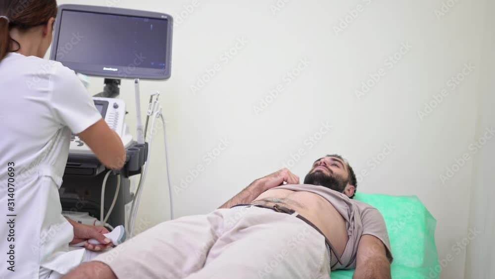 A young man is getting abdominal ultrasound scan by female doctor in medical uniform at hospital A young man is getting abdominal ultrasound scan by female doctor in medical uniform at hospital