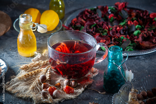 Red Hot Hibiscus tea in a glass mug on a wooden table among rose petals and dry tea custard with metallic heart