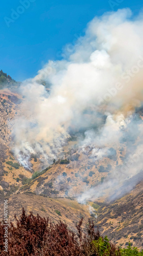 Vertical Aerial view of mountain top with vegetation and thick smoke against blue sky