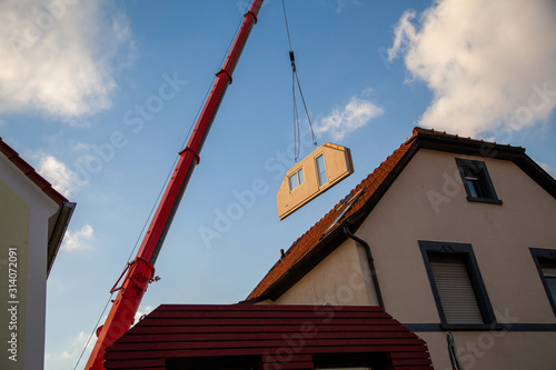 Prefabricated house part with windows between two houses is transported by the mobile crane for assembly