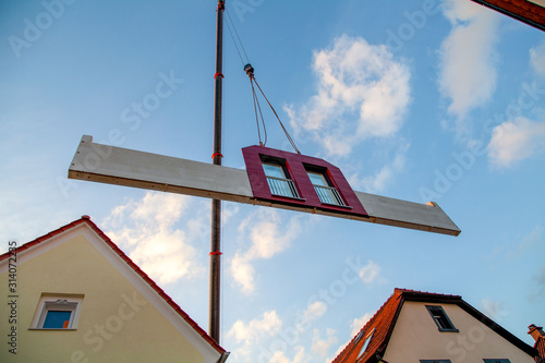 Prefabricated house part with two red windows is hoisted between two houses by the mobile crane for assembly