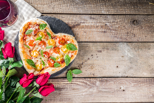 Pizza for Valentine day. Heart shaped homemade pizza margarita. Valentines day romantic menu concept. With wine bottle, roses flowers and and wineglass. Wooden background copy space