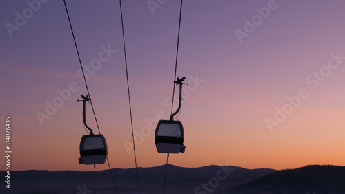modern ski lift cabin silhouettes move against sunset sky © wifesun