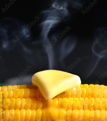 Ear of corn with melting butter and steam. Large, dark background.