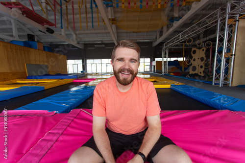 Fitness, fun, leisure and sport activity concept - Man sitting on a trampoline indoors