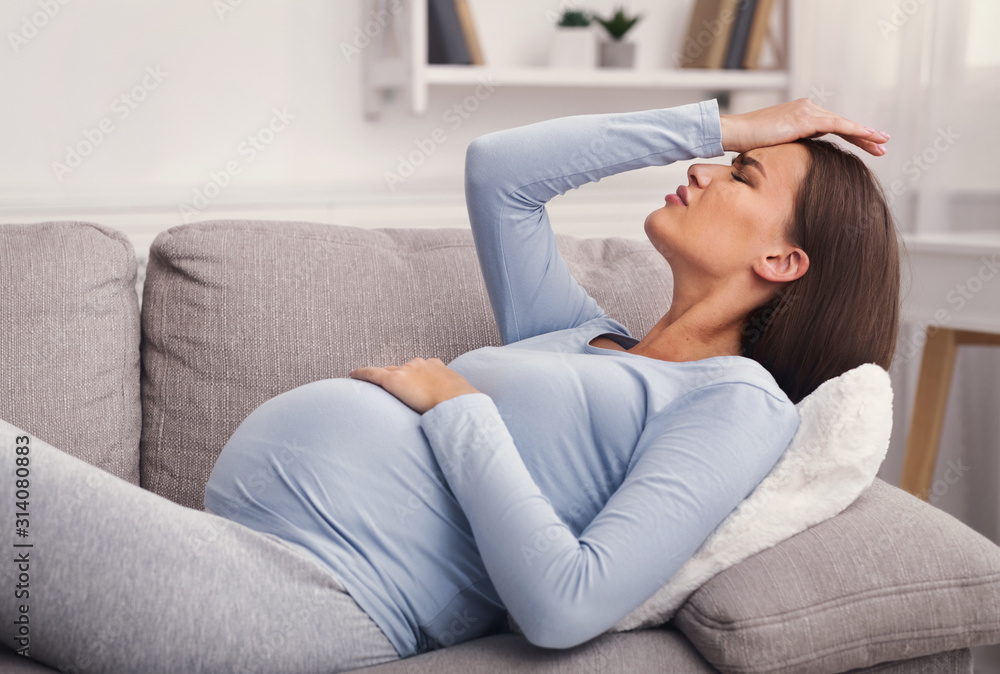 Pregnant Girl Suffering From Headache Lying On Couch At Home Pregnant Girl Suffering From Headache Lying On Couch At Home