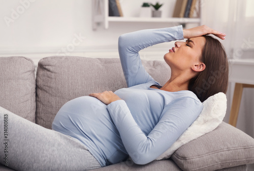 Pregnant Girl Suffering From Headache Lying On Couch At Home