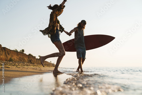 Photography Photo of caucasian delighted couple holding surfboard and making fun