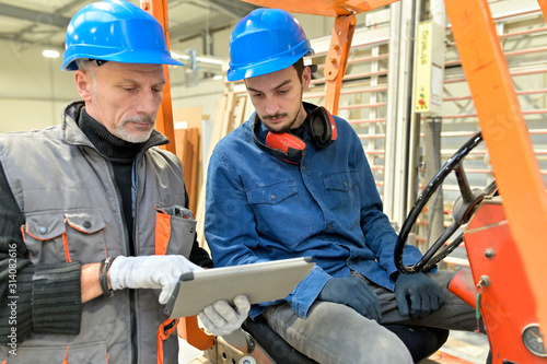 Man giving instructions to apprentice in warehouse, using cart photo