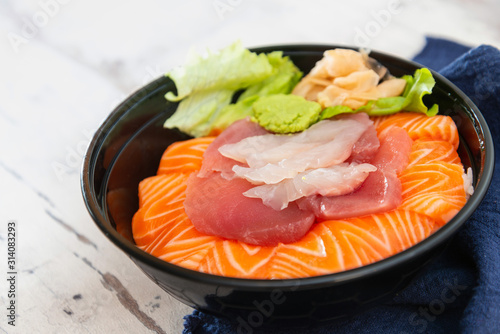 Slika na platnu Japanese Chirashi made with assortment of three raw fishes, salmon, tuna and cod fish served on white vinegary rice with Wasabi sauce and ginger slices on top in a bowl