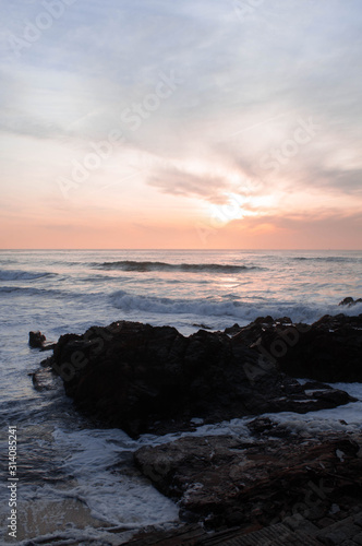 Sunset over the ocean, waves break down to rocks in the water