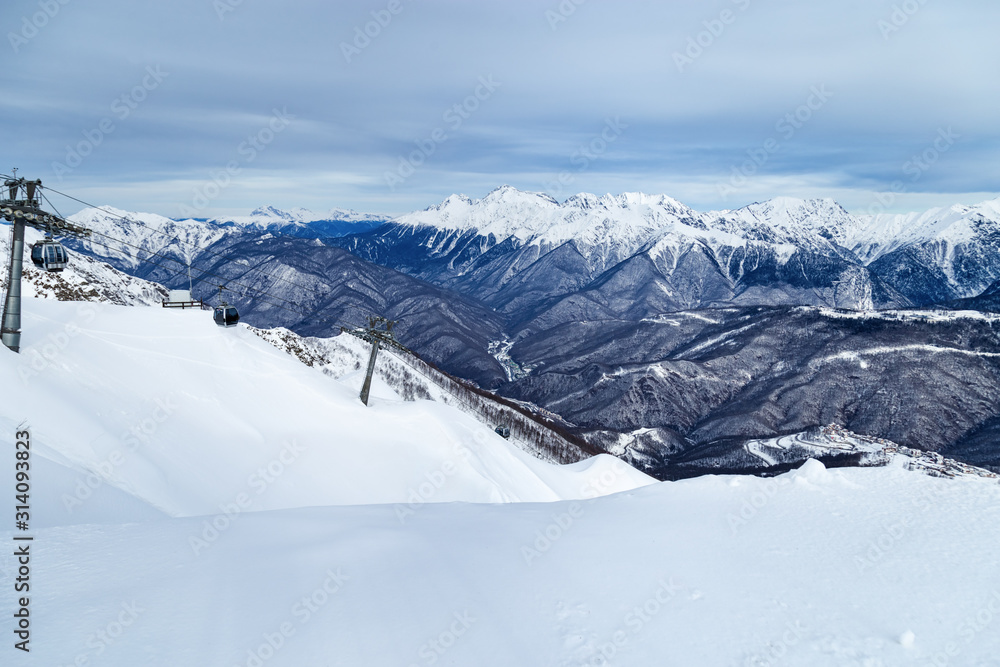Mountain slope in Rosa Khutor ski resort in Russia. Holidays and active rest in mountains. Winter cold season and blue clouds on sky.