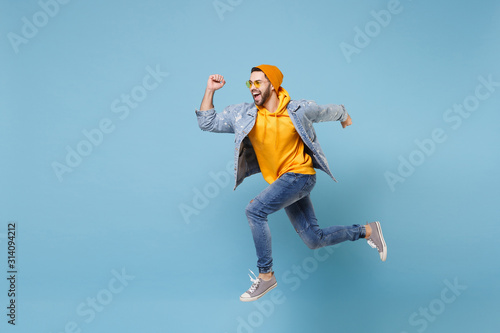 Cheerful young hipster guy in fashion jeans denim clothes posing isolated on pastel blue background studio portrait. People sincere emotions lifestyle concept. Mock up copy space. Jumping, running.