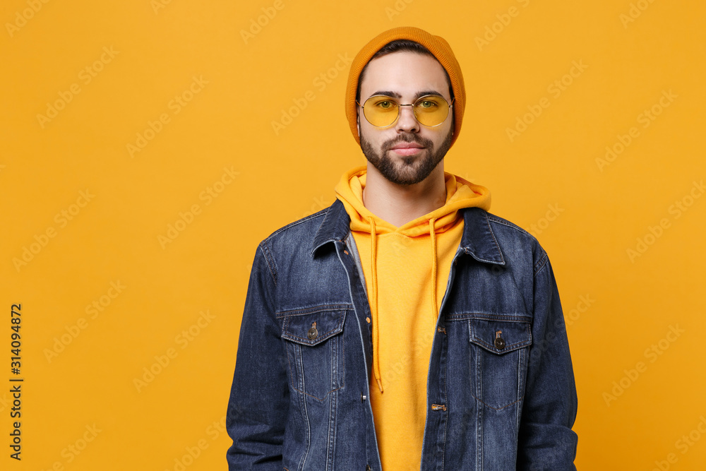 Handsome young hipster guy in fashion jeans denim clothes posing isolated on yellow orange background studio portrait. People sincere emotions lifestyle concept. Mock up copy space. Looking camera. Handsome young hipster guy in fashion jeans denim clothes posing isolated on yellow orange background studio portrait. People sincere emotions lifestyle concept. Mock up copy space. Looking camera.