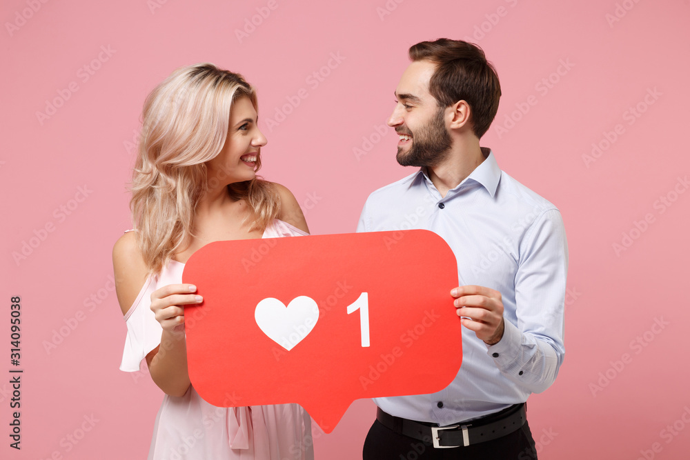 Smiling young couple two guy girl in party outfit celebrating posing  isolated on pink background. Valentine's Day Women's Day birthday holiday  concept. Hold huge like sign from Instagram heart form. Stock Photo