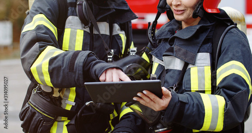 Photography Portrait of two firefighters in fire fighting operation, fireman in protective clothing and helmet using tablet computer in action fighting