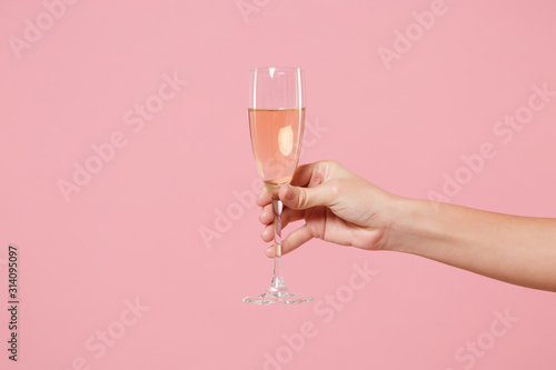 Close up cropped photo of female hold in hand glass of champagne isolated on pastel pink wall background. Copy space advertising mock up. Valentine's Day Women's Day birthday holiday party concept.