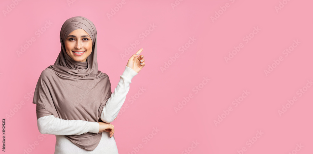Smiling arabian girl pointing at copy space over pink background - obrazy, fototapety, plakaty 