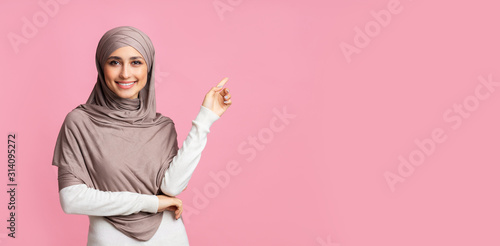 Smiling arabian girl pointing at copy space over pink background photo