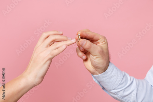 Close up cropped photo of female and male hold, putting proposal ring on finger isolated on pink background. Copy space advertising mock up. Valentine's Day Women's Day birthday holiday party concept.