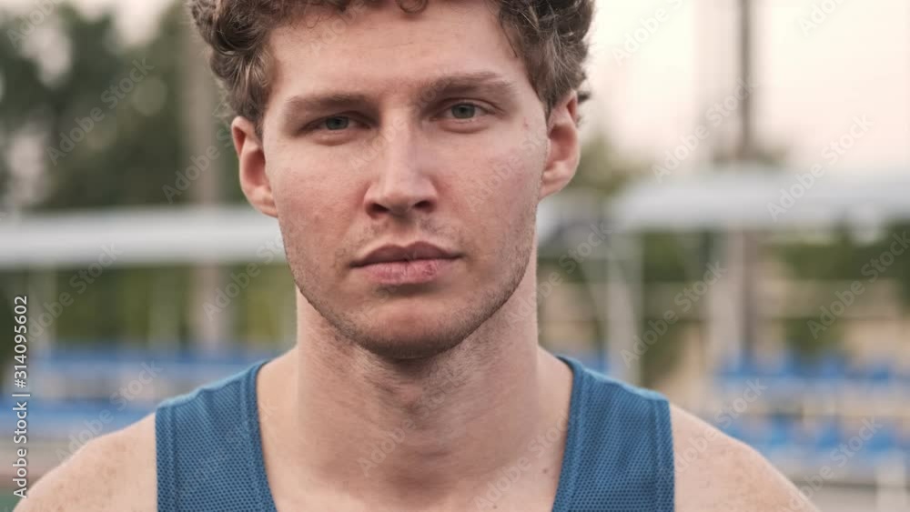 Close up view of pleased curly handsome man looking at the camera and posing on stadium outdoors Close up view of pleased curly handsome man looking at the camera and posing on stadium outdoors