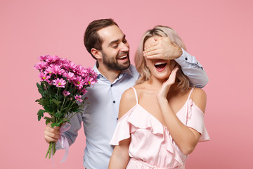 Cheerful young couple two guy girl in party outfit celebrating isolated on pastel pink background. Valentine's Day Women's Day birthday holiday concept. Hold bouquet of flowers, cover eyes with hand.