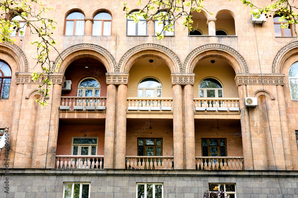 Obraz premium Fragment of building with small balconies with arches, columns and stone carvings. Yerevan, Armenia
