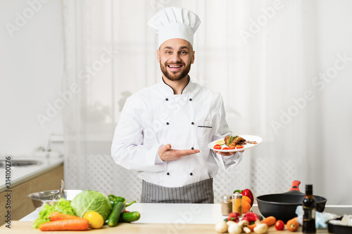 Cook Man Holding Plate With Chicken Presenting Dish In Kitchen