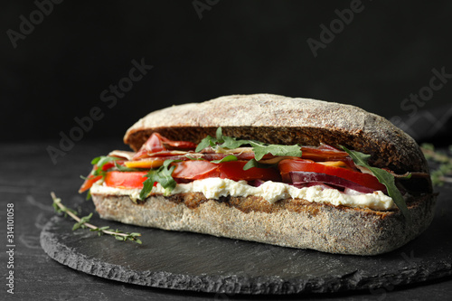 Delicious sandwich with fresh vegetables and prosciutto on black table photo