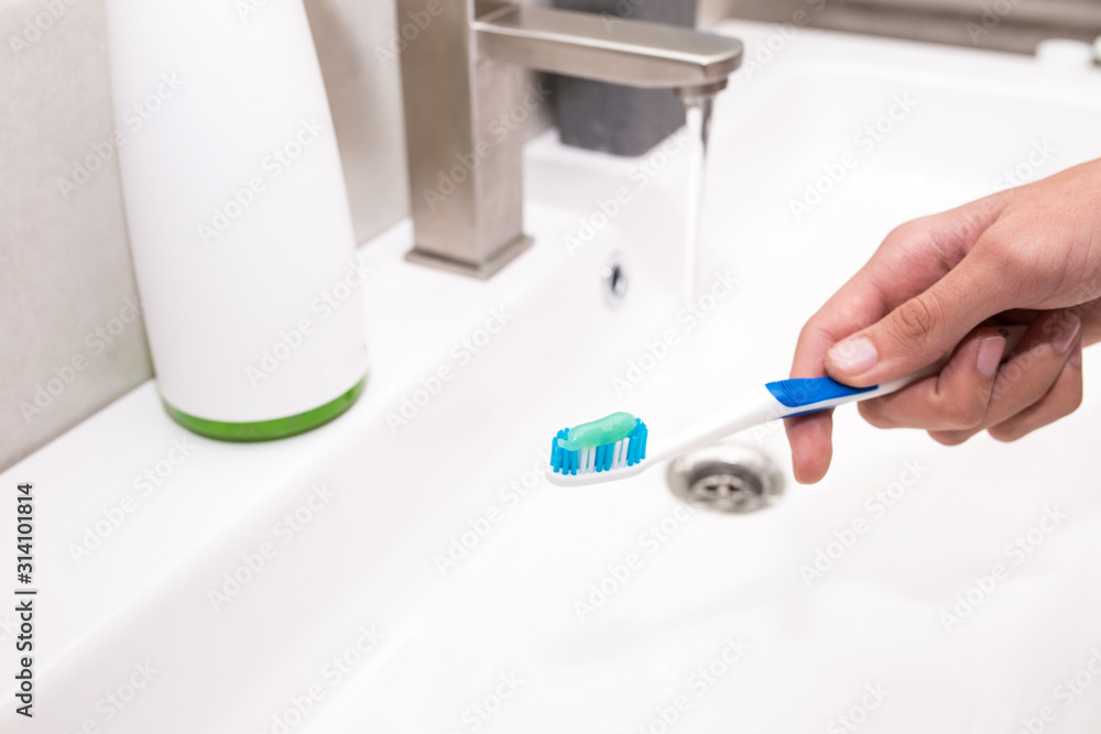 Toothbrush with toothpaste in the guy's hand on the background of the washbasin. Toothbrush with toothpaste in the guy's hand on the background of the washbasin.