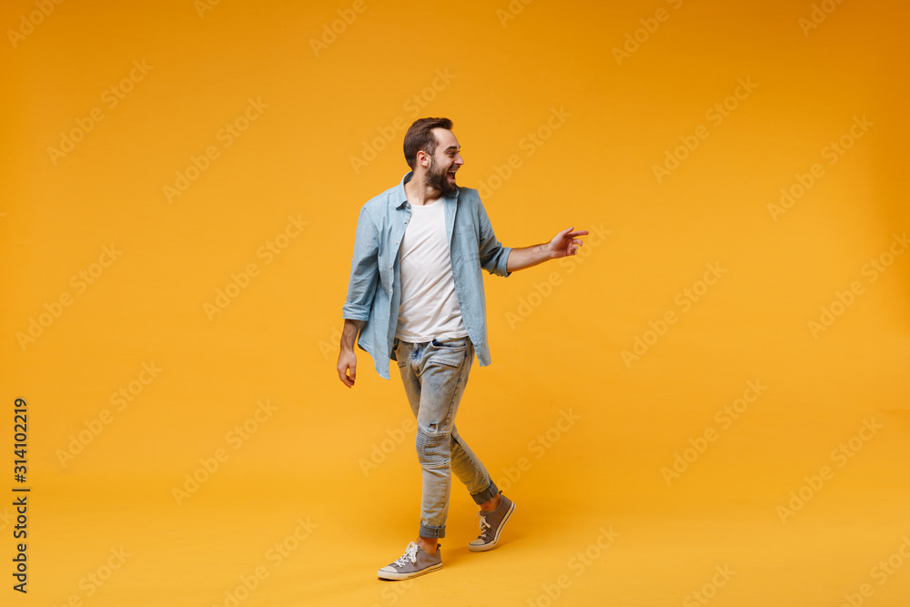 Fototapeta premium Excited young bearded man in casual blue shirt posing isolated on yellow orange background studio portrait. People emotions lifestyle concept. Mock up copy space. Looking, pointing index finger aside.