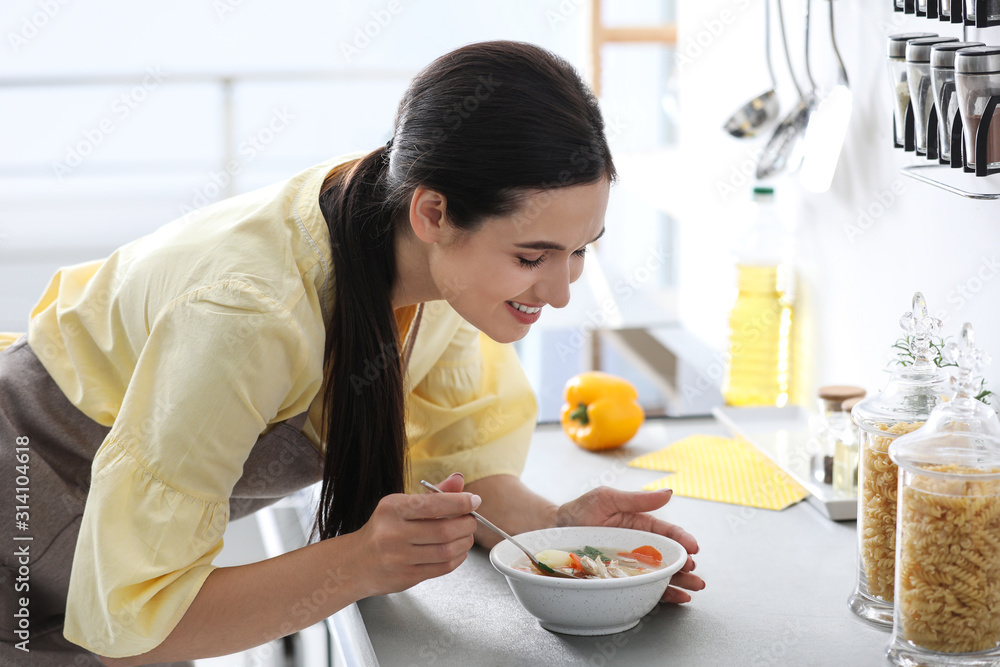 Young woman eating tasty vegetable soup at countertop in kitchen Young woman eating tasty vegetable soup at countertop in kitchen