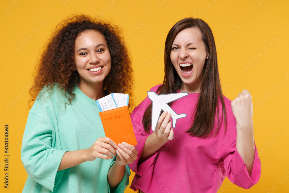 Two women friends european american girls in pink green clothes posing isolated on yellow background. People lifestyle concept. Mock up copy space. Hold passport ticket airplane doing winner gesture. Two women friends european american girls in pink green clothes posing isolated on yellow background. People lifestyle concept. Mock up copy space. Hold passport ticket airplane doing winner gesture.