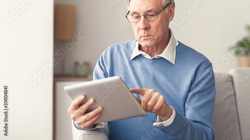 Senior Gentleman Using Tablet Sitting On Sofa At Home, Panorama
